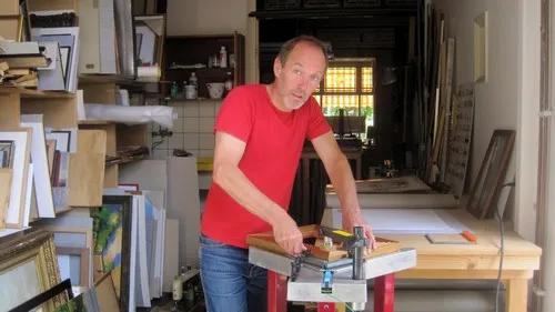 Jacob Loef aan het werk aan een lijst in zijn werkplaats, omringd door lijsten en prenten